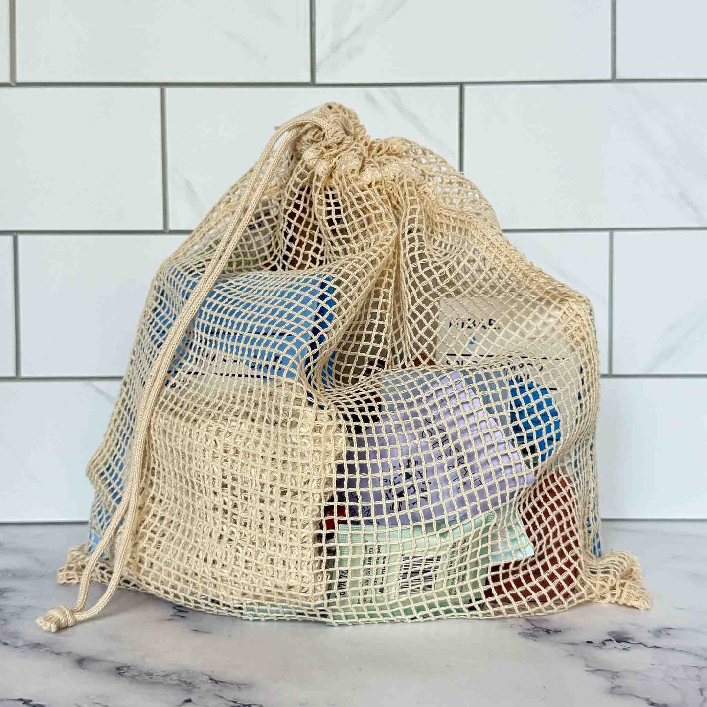 Mesh drawstring bag filled with our travel kit products against a tiled wall background